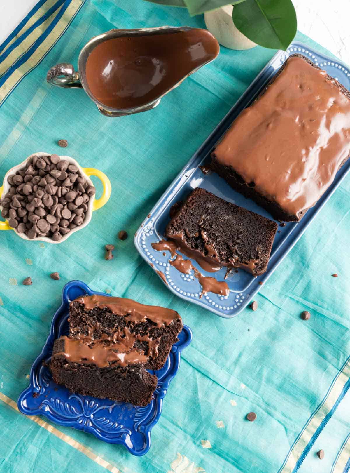 Brownie cake on a blue table cloth and chocolate chips on the side.