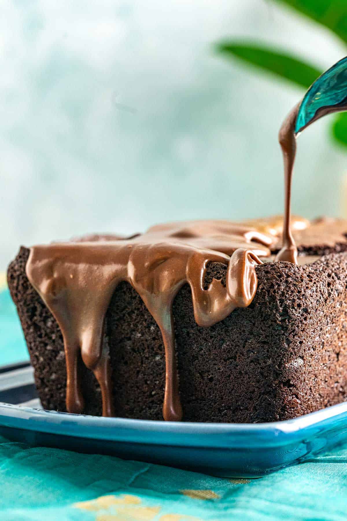 Ganache pouring on the brownie bread in a rectangle blue plate.