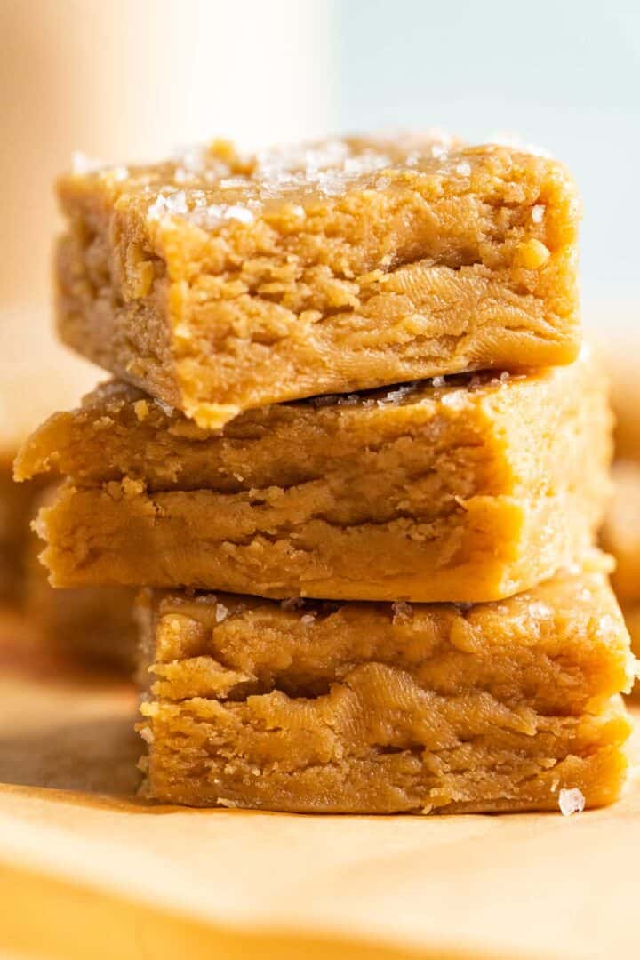 close shot of three peanut butter fudge sitting on each other and showcasing the texture and sea salt flakes.