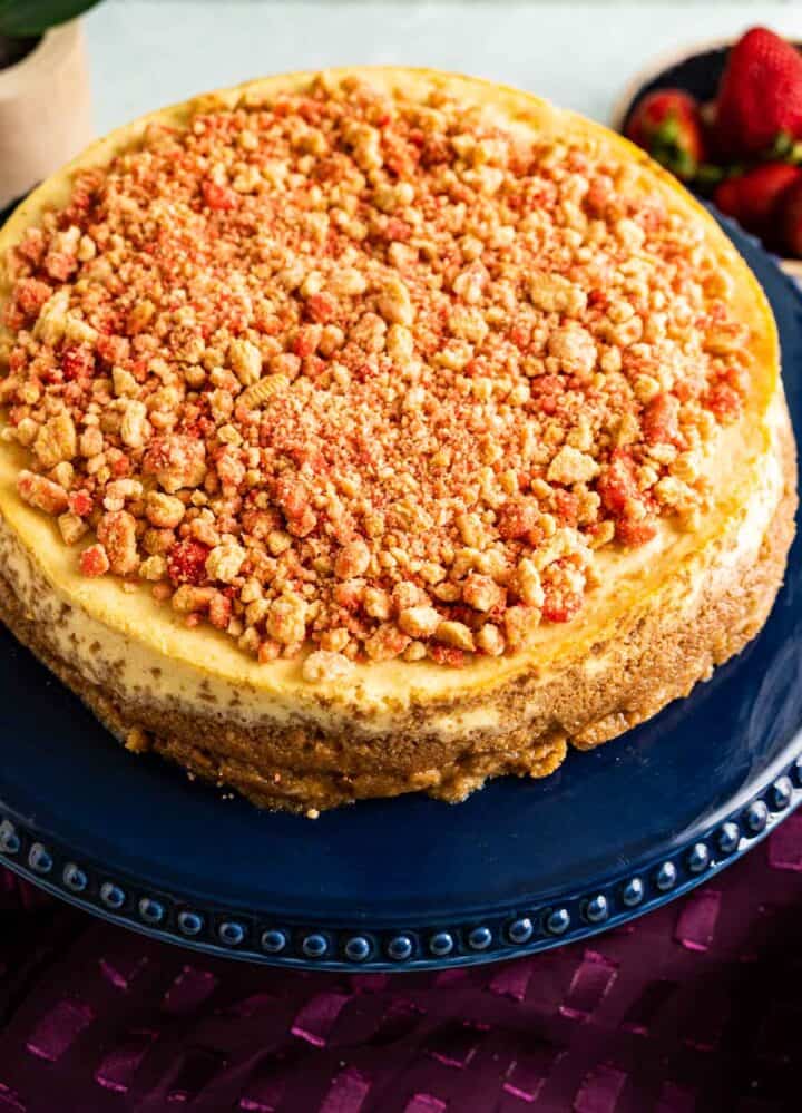 overhead close shot of strawberry crunch cheesecake sitting on a navy blue cake plate with a magenta table cloth in the backdrop.