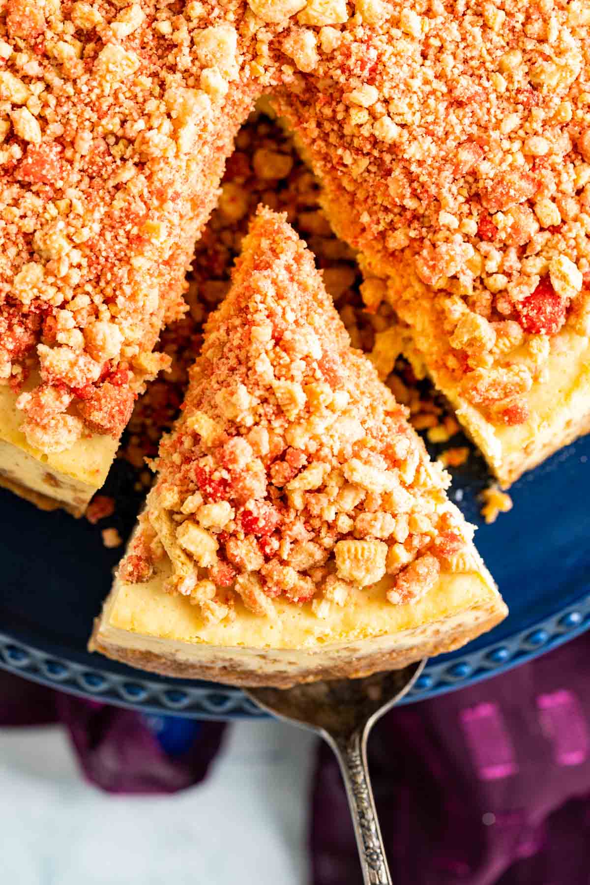 a cut slice of strawberry crunch cheesecake on an antique copper cake spoon over the cake plate.