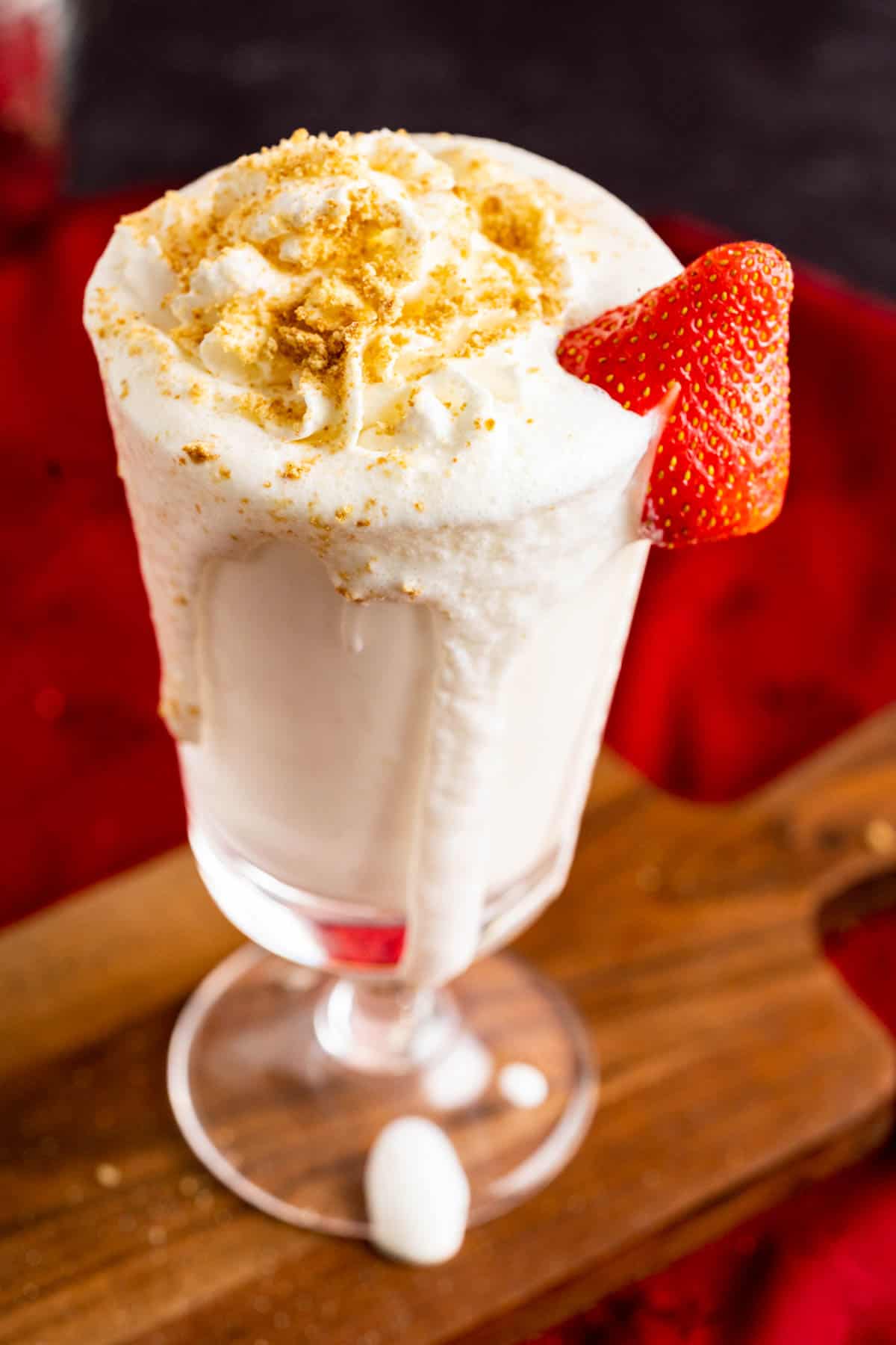 Cheesecake milkshake dripping down the glass placed on a wooden piece.