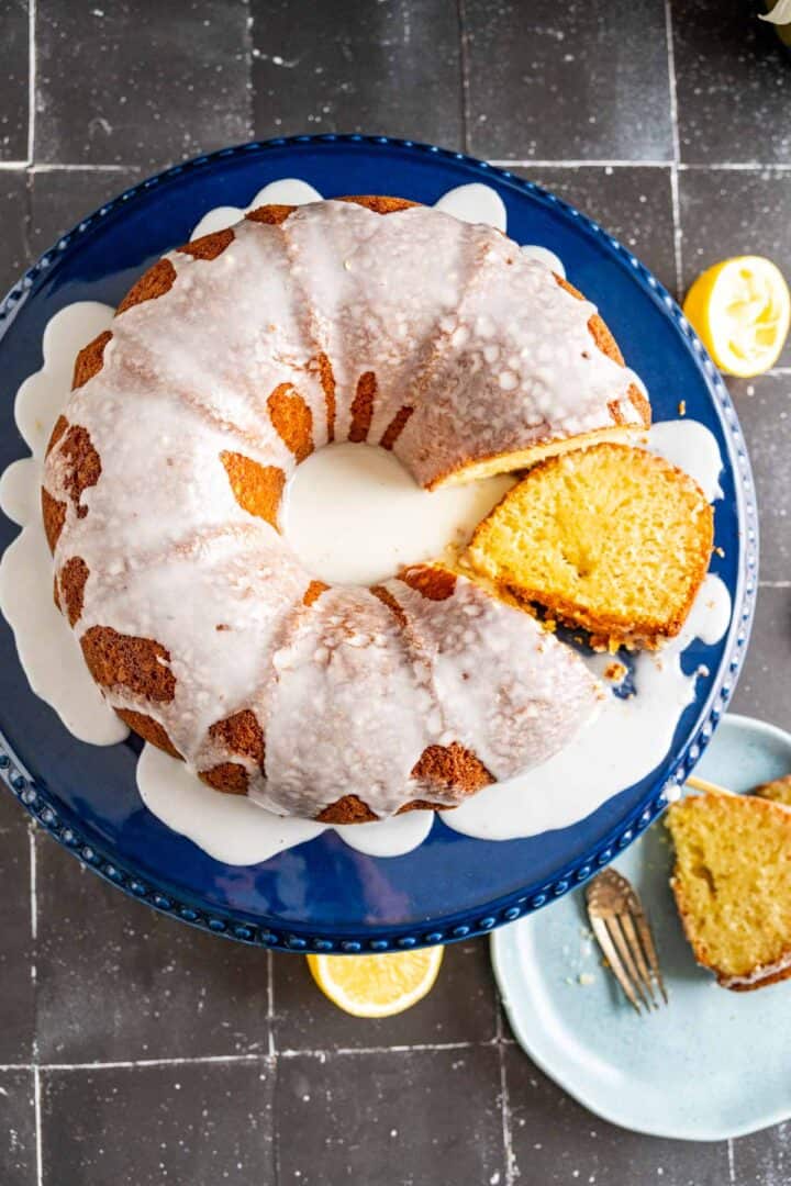 over the head shot of lemon cake placed on a blue cake plate with lemon pieces scattered on black tiles.