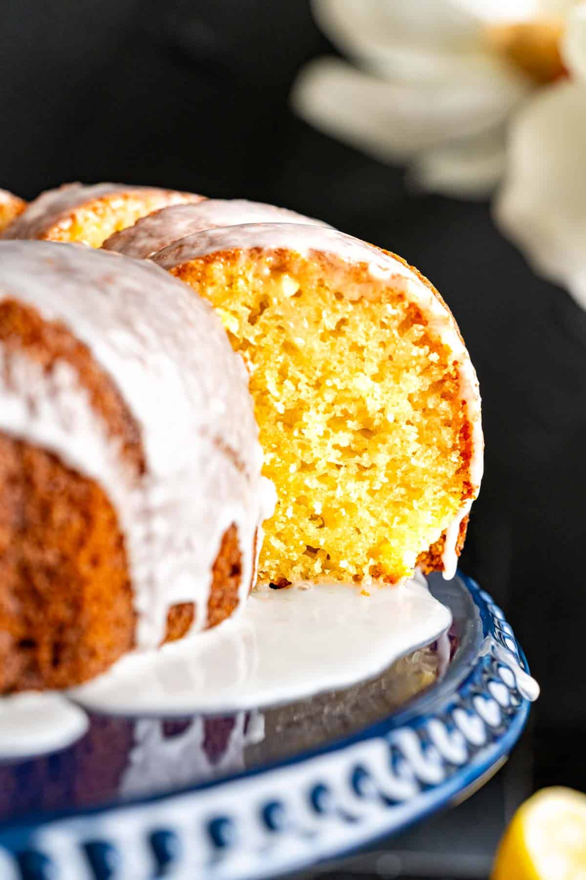 texture of a single cake piece of lemon yogurt cake placed along the lemon yogurt cake on a navy blue cake plate.