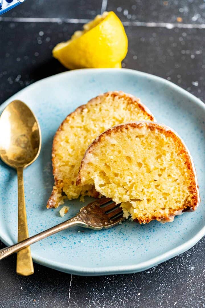 two slices of lemon cake with a golden fork and golden spoon placed on a blue plate.