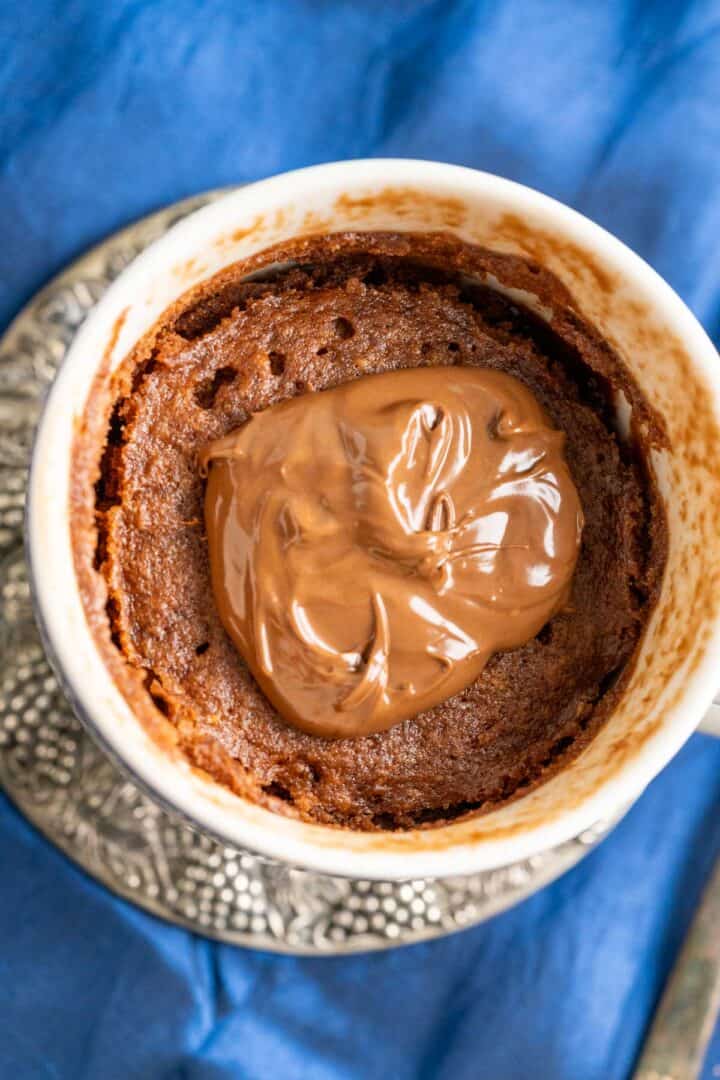 overhead shot of the nutella cake in a mug placed on a silver antique plate over a royal blue table cloth.