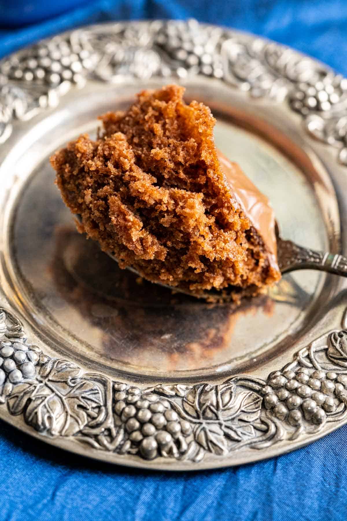 A bite of nutella mug cake in a spoon placed in a silver antique plate.