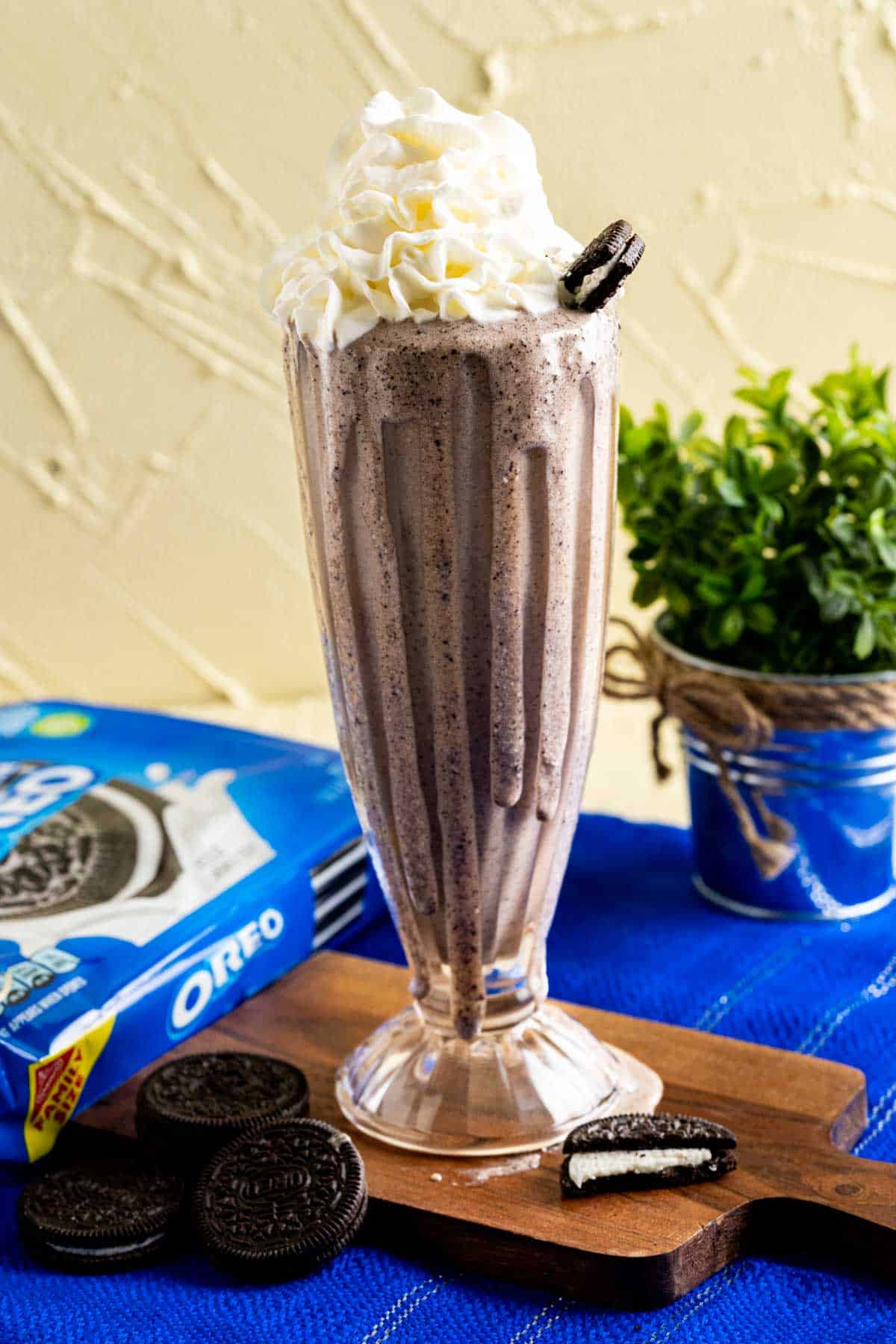 A tall glass of Oreo Banana Milkshake on a wooden piece.