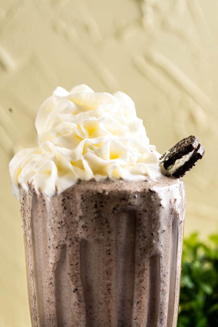 close shot of the oreo banana milkshake in a glass with whipped cream and a piece of oreo cookies.