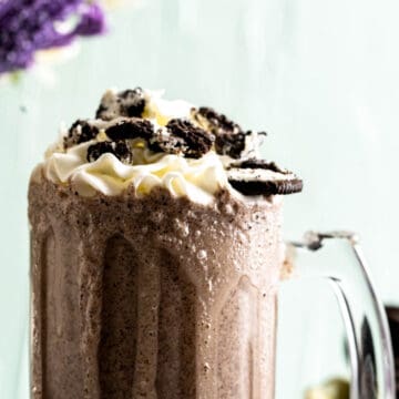 oreo shake in a tall transparent glass with crushed oreos on the top.