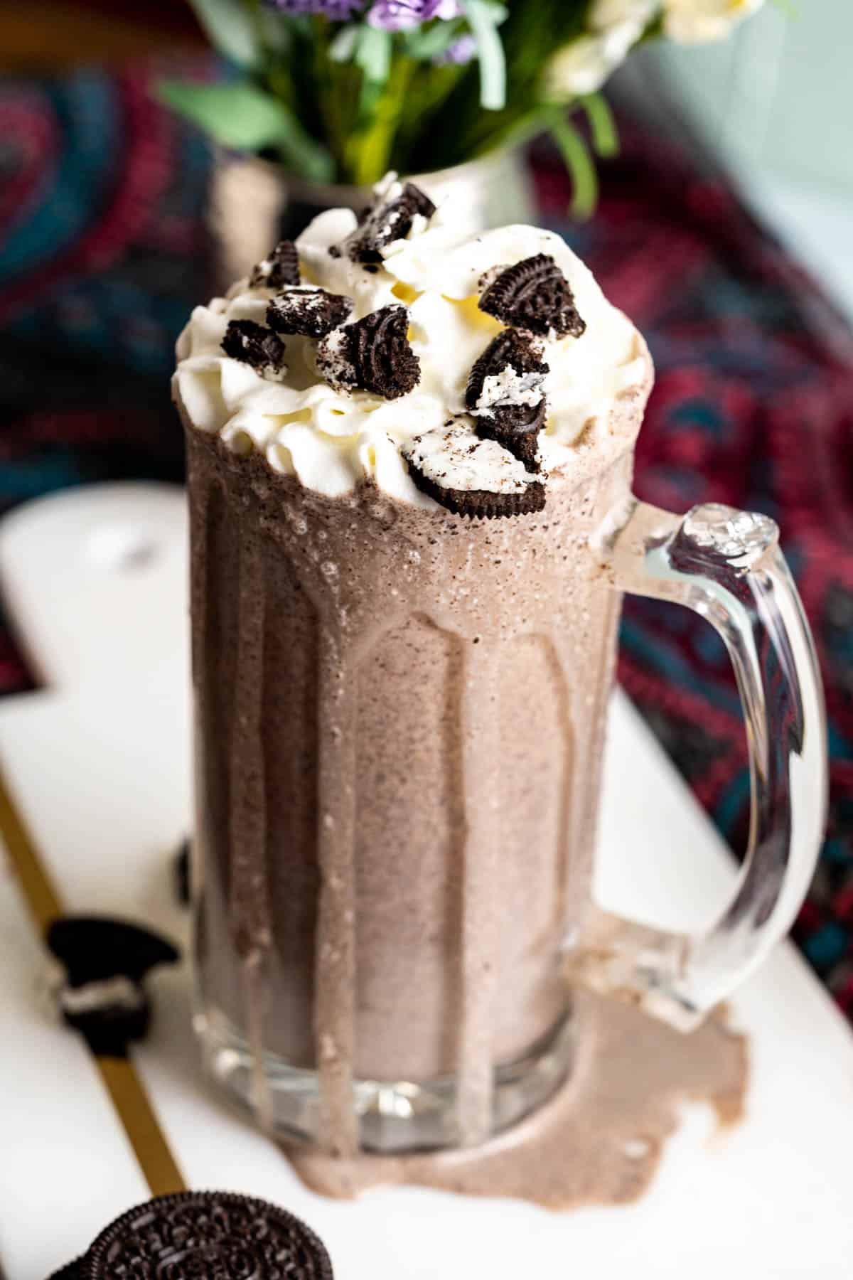 Milkshake with Oreos in a glass with a dollop of whipped cream and crushed Oreos.