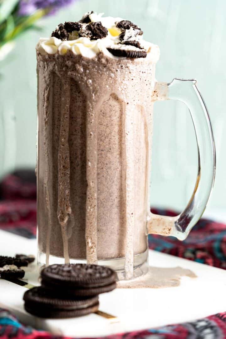 tall glass of dripping oreo shake with dollop of whipped cream on the top and crushed oreo cookies.