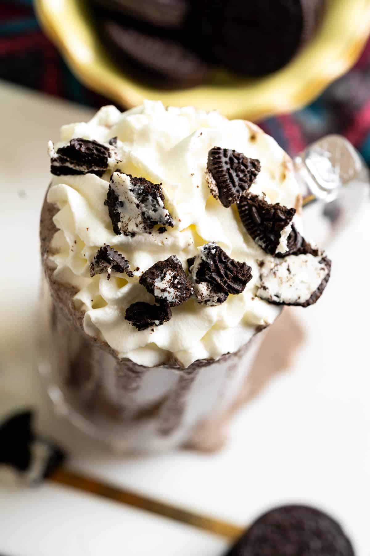 Milkshake with crumbled Oreos on whipped cream in a tall glass on a white marble plate.