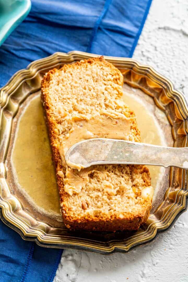 a slice of peanut butter quick bread on golden plate with silver knife and peanut butter on it.