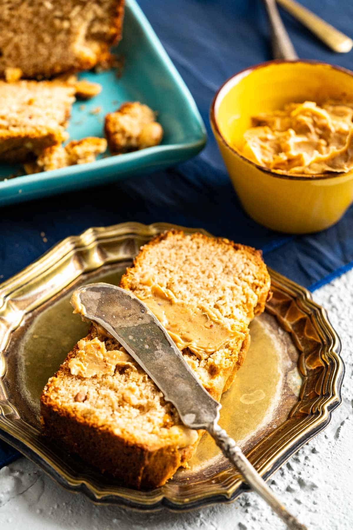 Peanut butter applied with a knife on a bread piece and an old silver knife sitting on the slice.