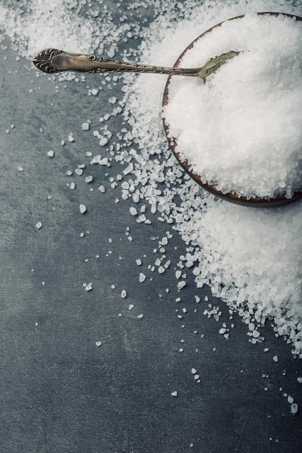 salt in a wooden bowl with a silver spoon in it.