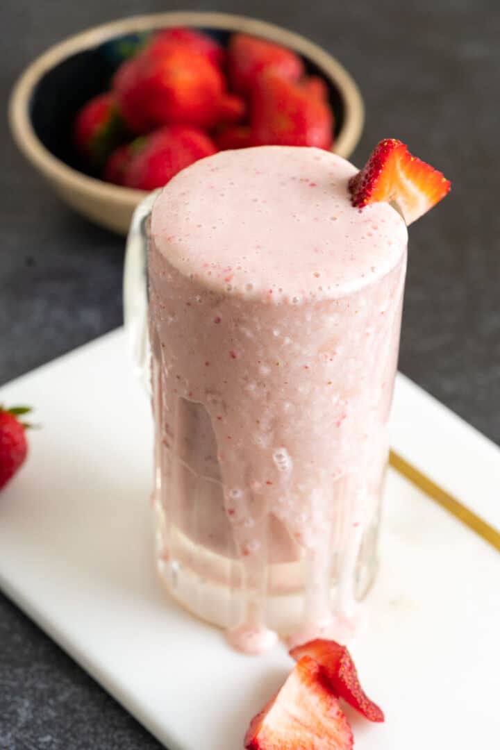 close shot of strawberry banana milkshake with strawberries around on the table.