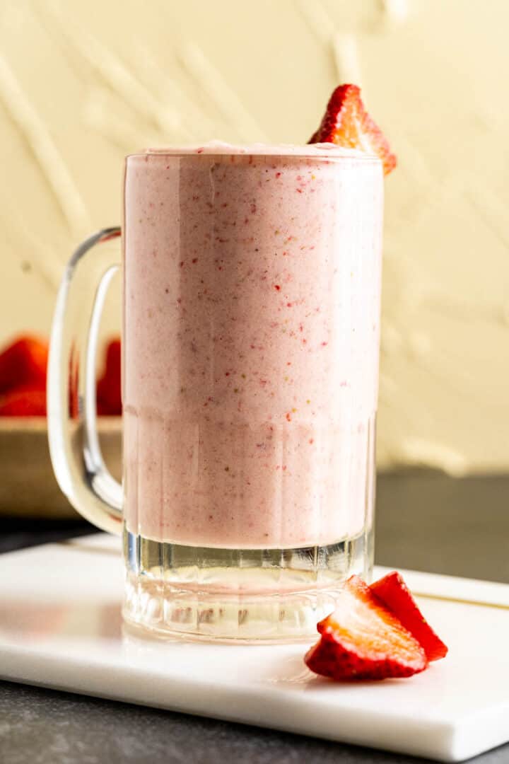 a glass full of milkshake sitting on a white marble plate.