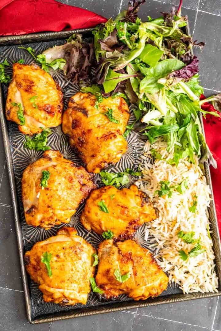 overhead shot of six buffalo chicken thighs on an antique silver tray with rice and salad on the side.