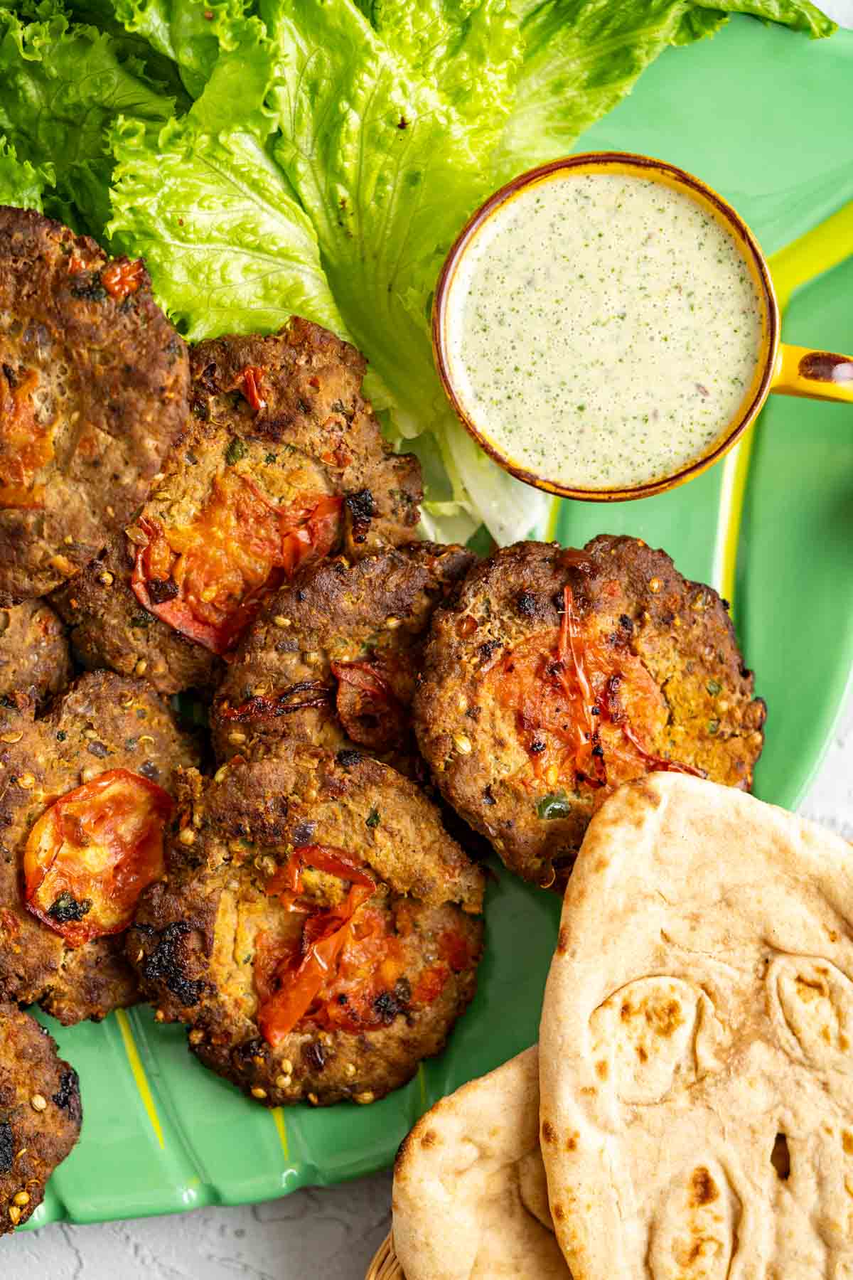 Fried chapli kabab sitting in a plate along with salad leaves, mint chutney and naans.