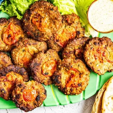 chapli kababs set in a green plate with roti on the side.