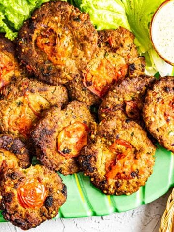 chapli kababs set in a green plate with roti on the side.