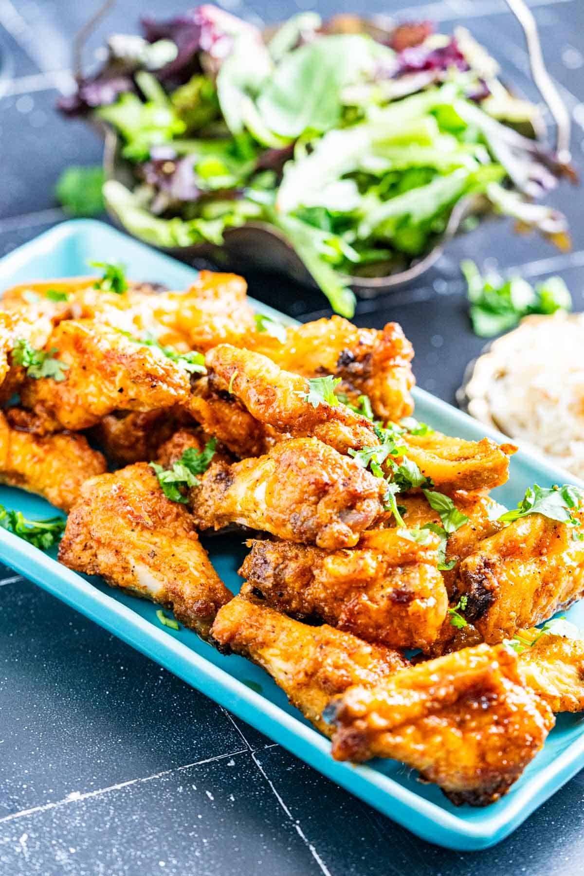 Honey lemon pepper wings on a blue plate with salad plate in the backdrop.