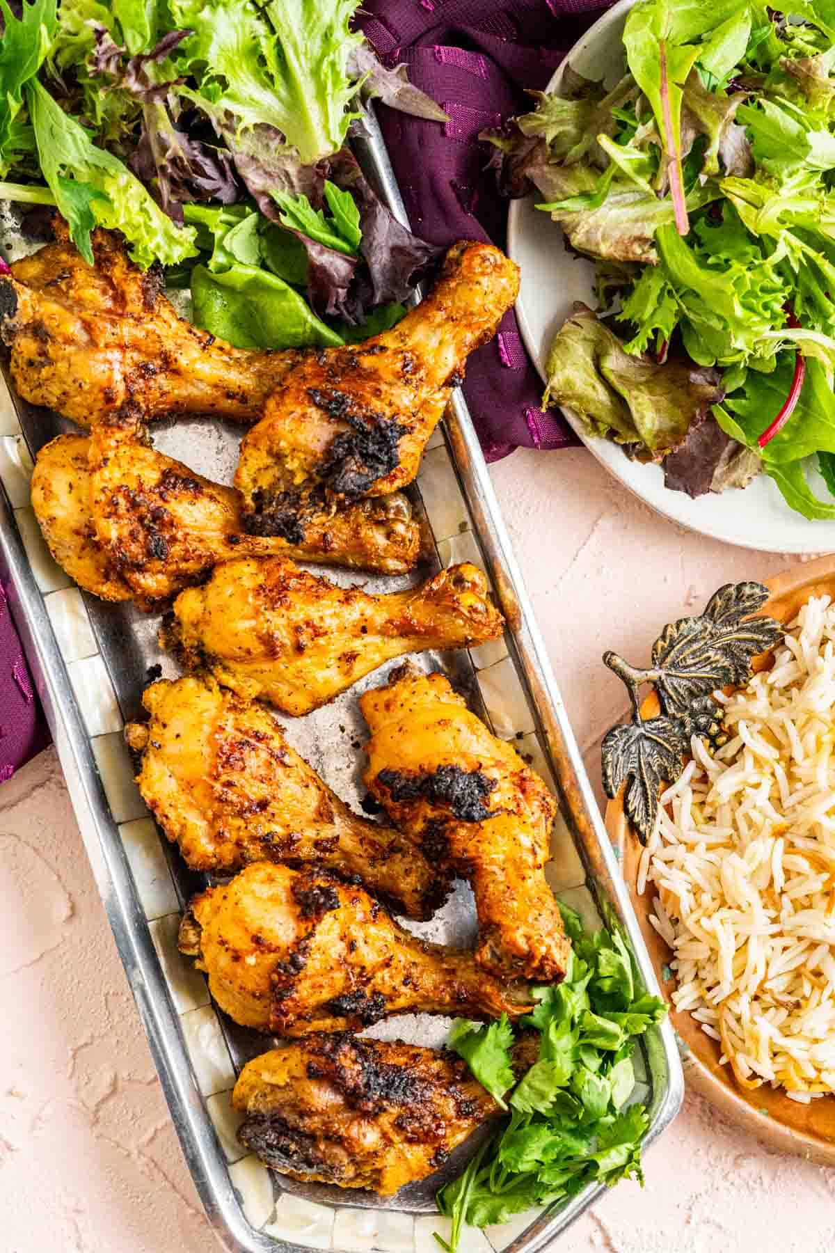 Lemon drumsticks in a silver tray along with a bowl of rice on the table.