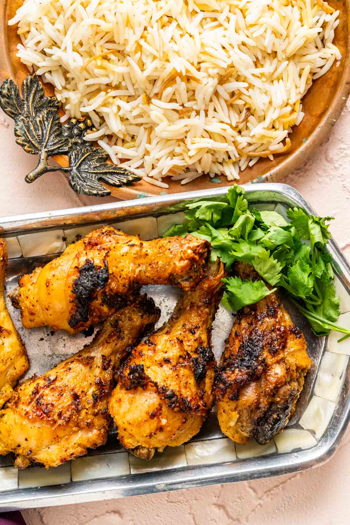 Chicken legs in a silver plate with rice and cilantro on the side.