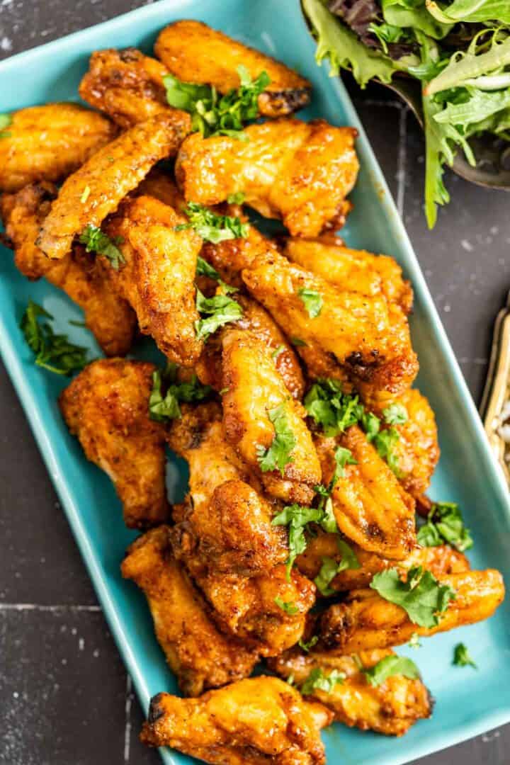 close overhead shot of chicken wings in a blue plate with sprinkled coriander over it.