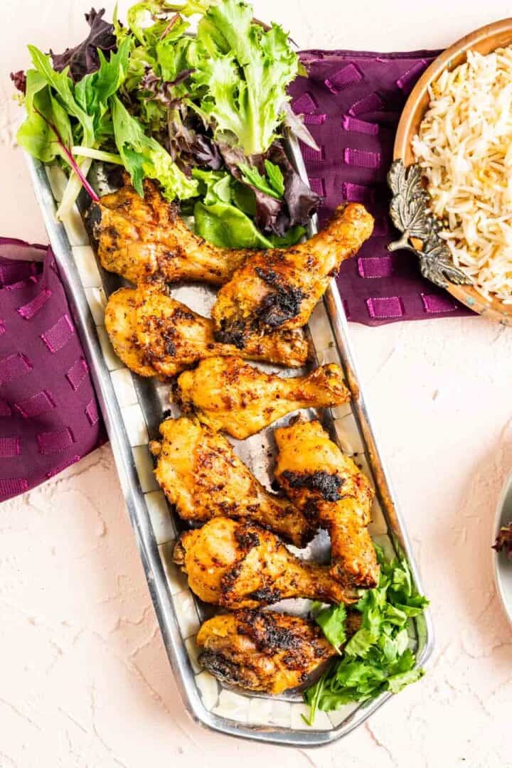 overhead shot of chicken pieces in a silver antique long plate with white boiled rice on the side.