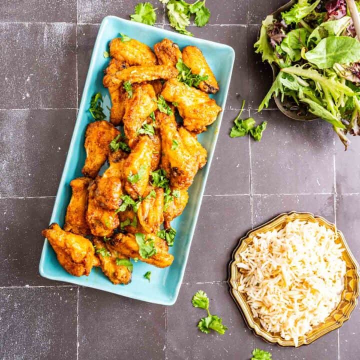 overhead shot of honey lemon chicken wings in a rectangular blue plate with salad and rice on the side.