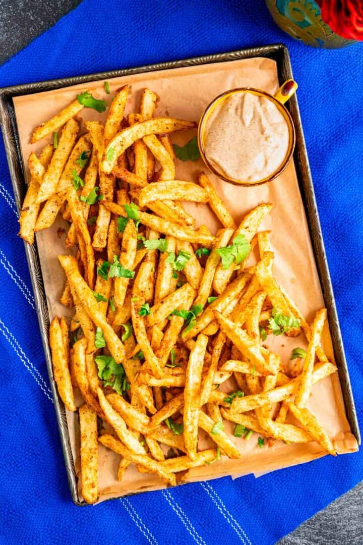 french fries spread on an antique silver tray with peri peri sauce on the side.