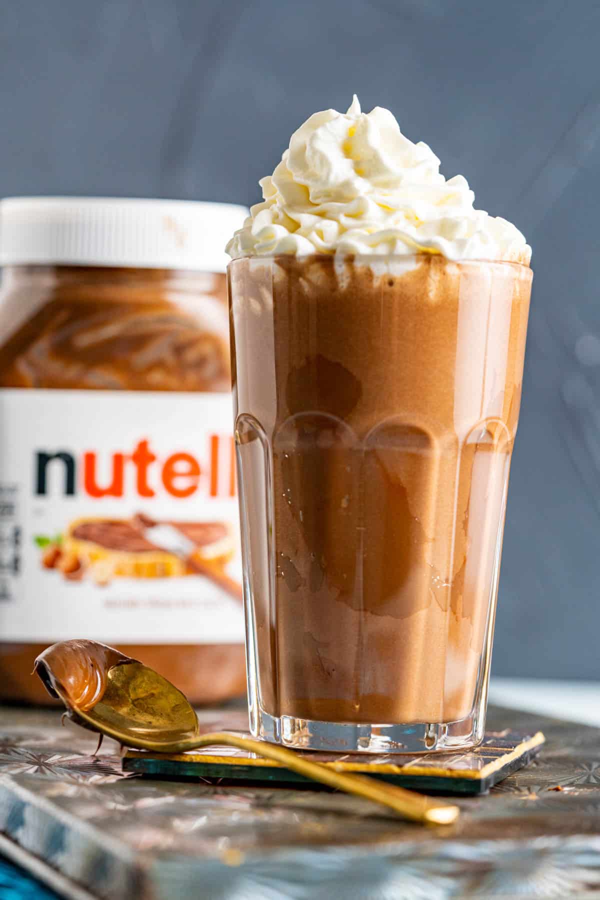 Nutella milkshake in a big glass with a golden spoon on the side with nutella in it.