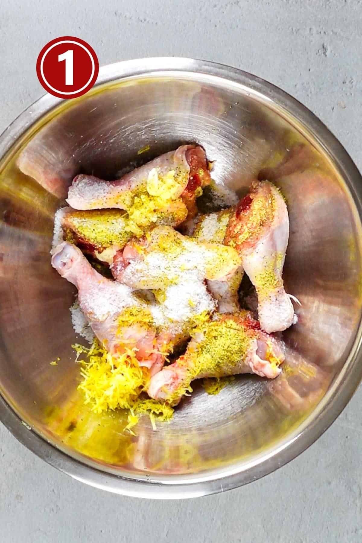 Chicken pieces with spices in a large steel bowl.