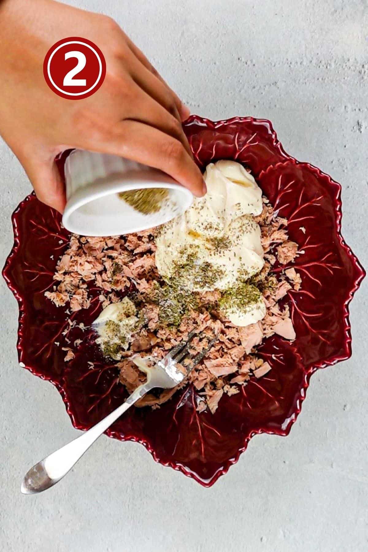 Adding the spices and mayonnaise to tuna in a bowl.