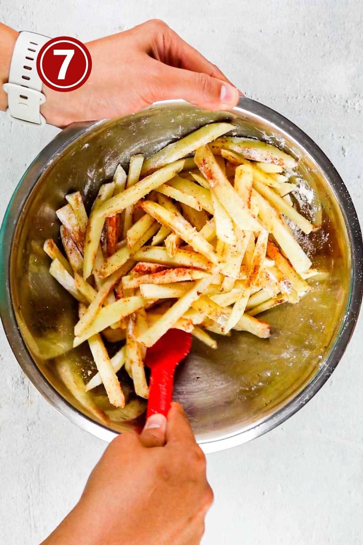 Tossing the spices in the potatoes in a large steel bowl.