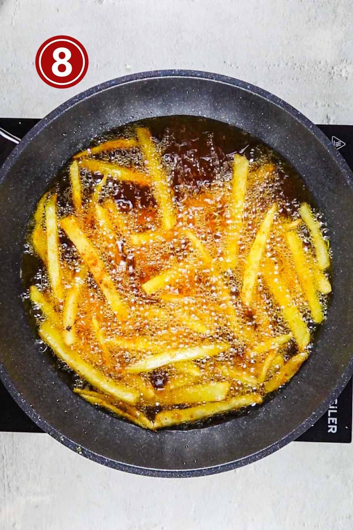 Potatoes being fried at a high temperature in a frying pan.