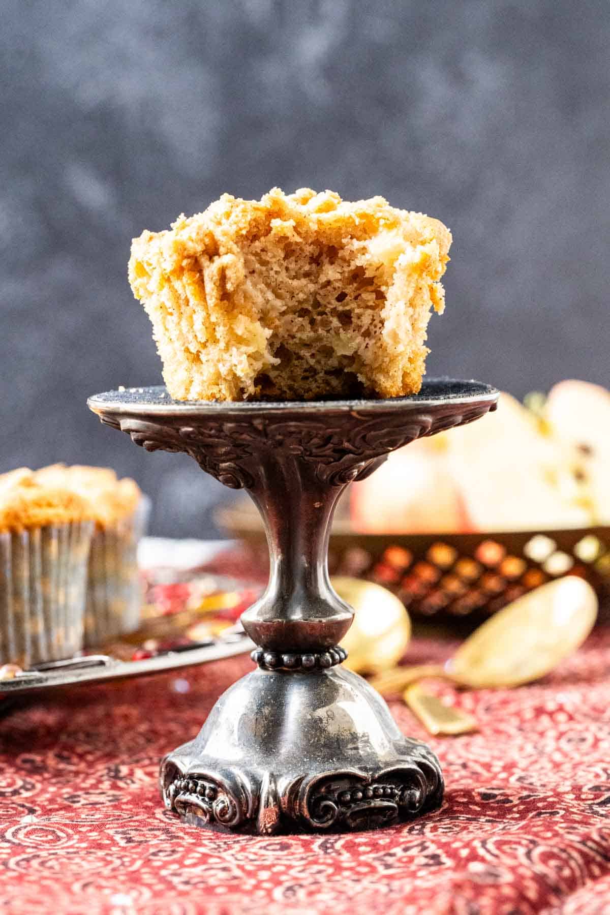 Muffin on a decorative silver stand showing apple chunks inside.