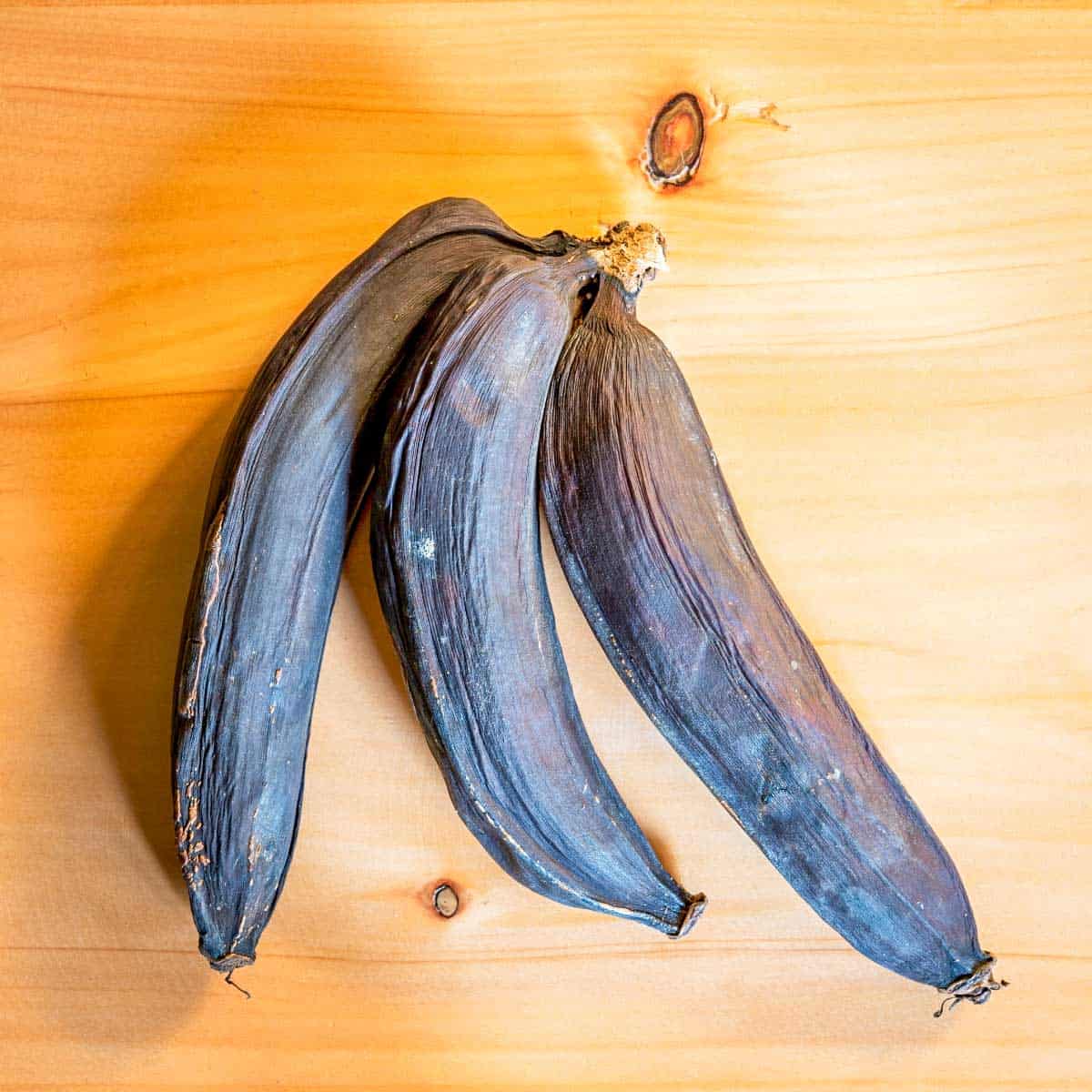 three blackened bananas on wooden surface.