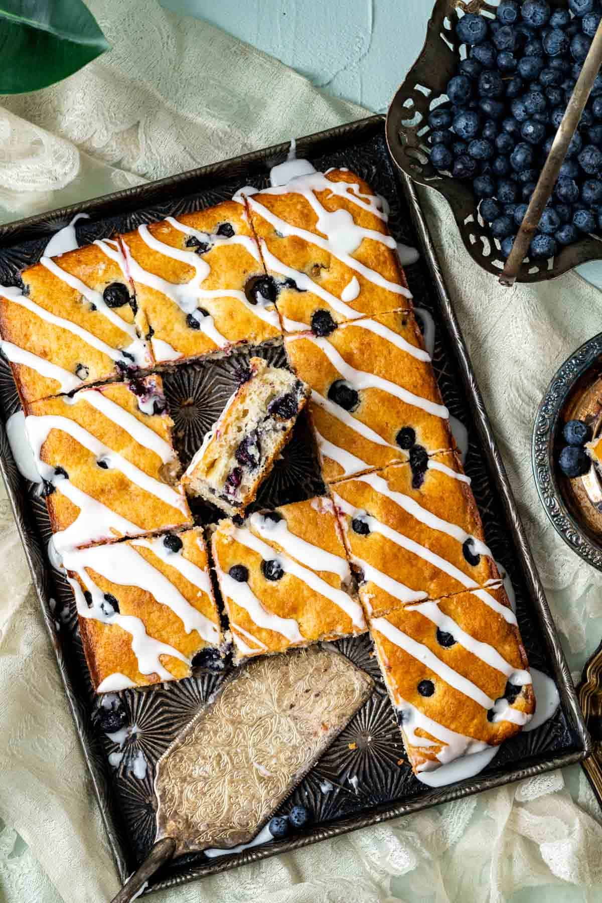 from the top shot of blueberry cake pieces in the sheet pan with blueberries around.