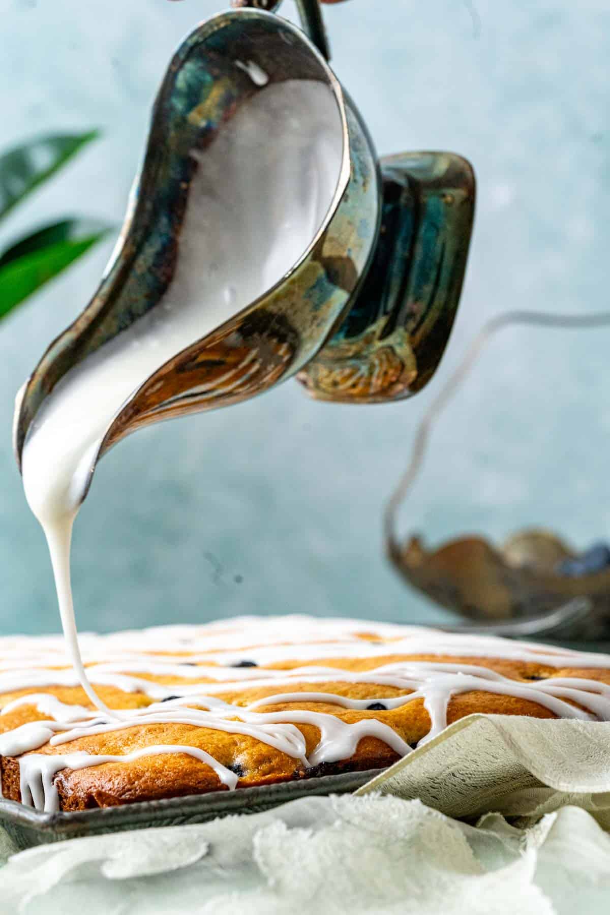 pouring lemon glaze over the blueberry cake.