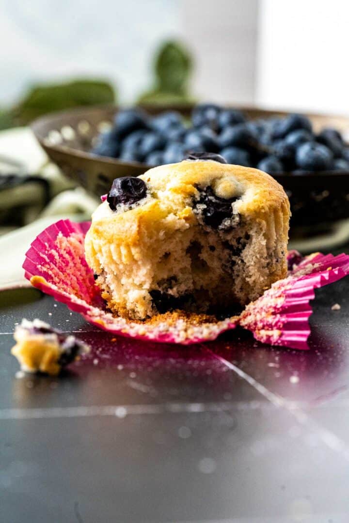 a muffin sitting on a black table showcasing the blueberries inside.