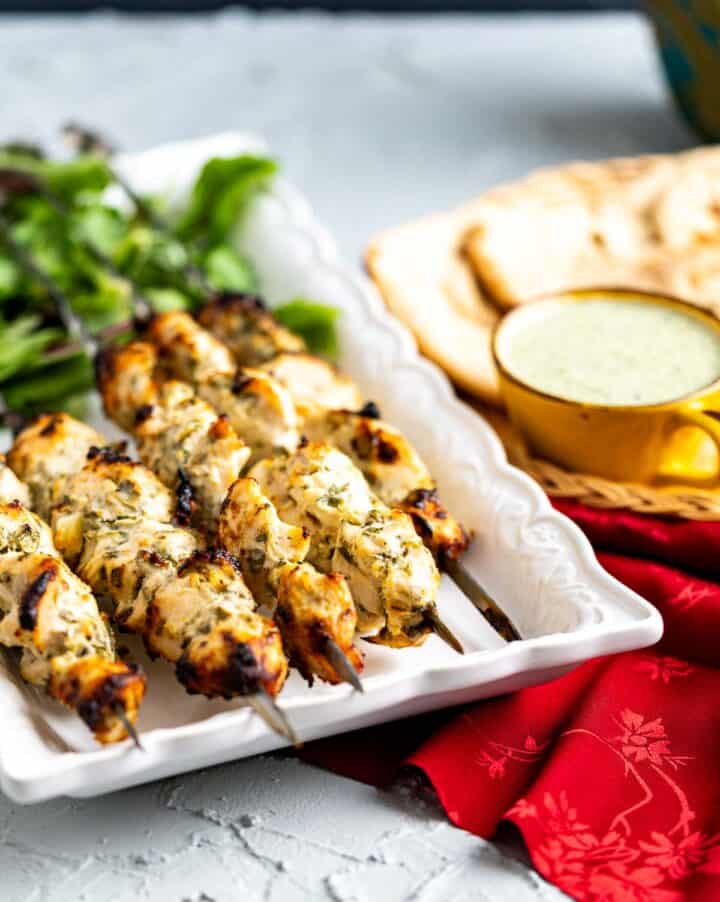 chicken tikka boti threaded in steel skewers and placed on a plate over red table cloth.