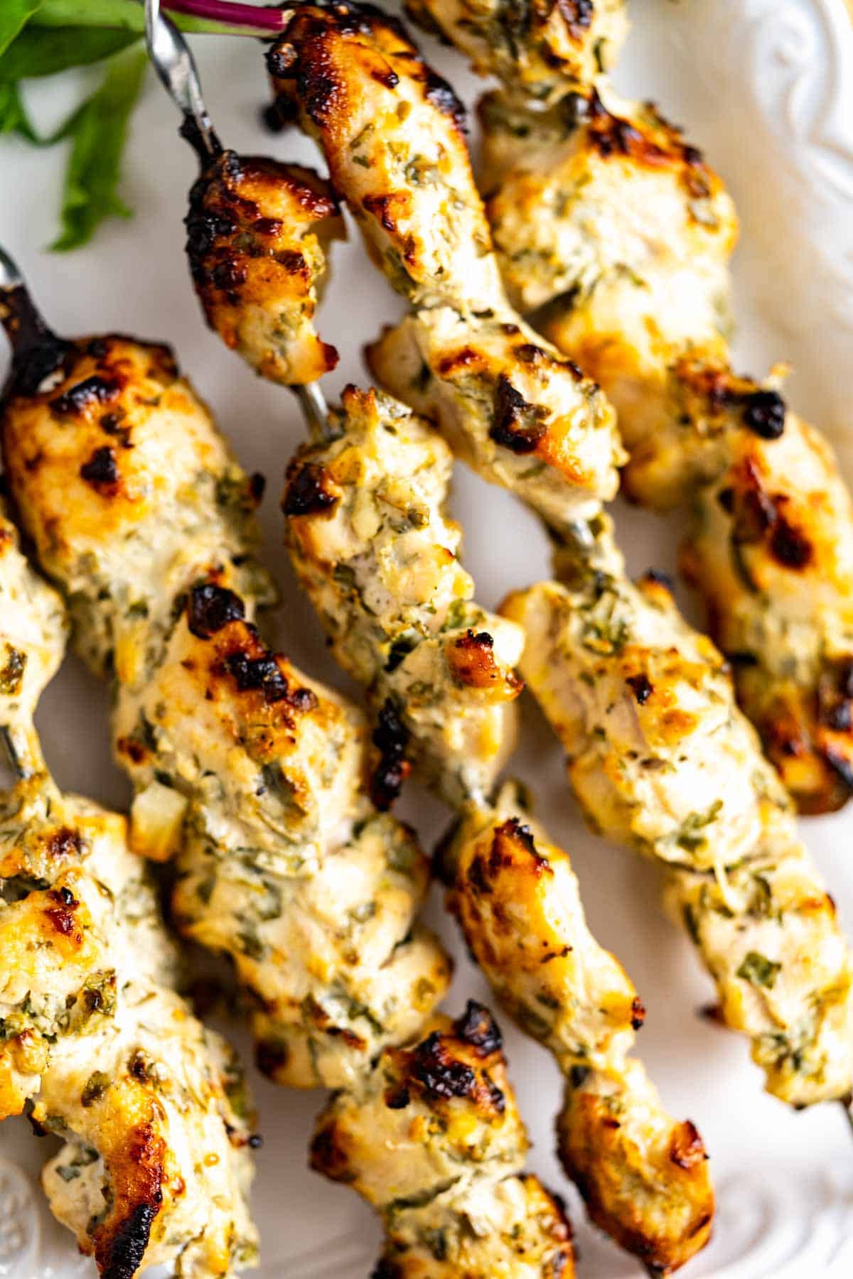 Cooked malai chicken boti skewers sitting on a white plate.