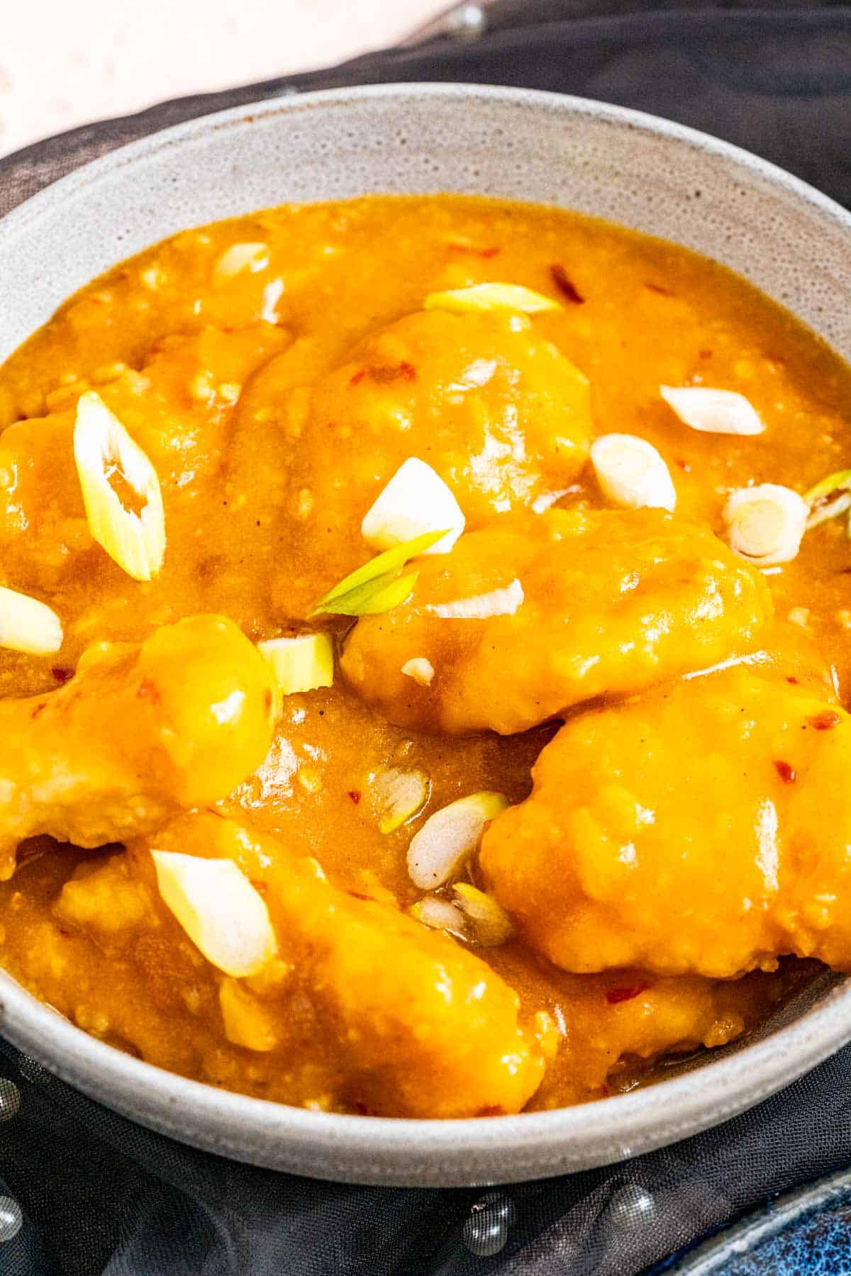 Orange chicken with sprinkled green onion served in a gray bowl.