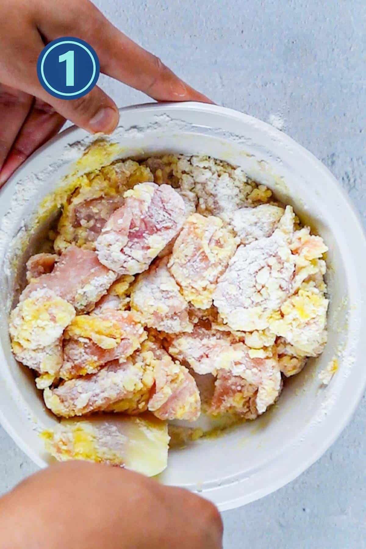 Coating chicken pieces with spices in a bowl.