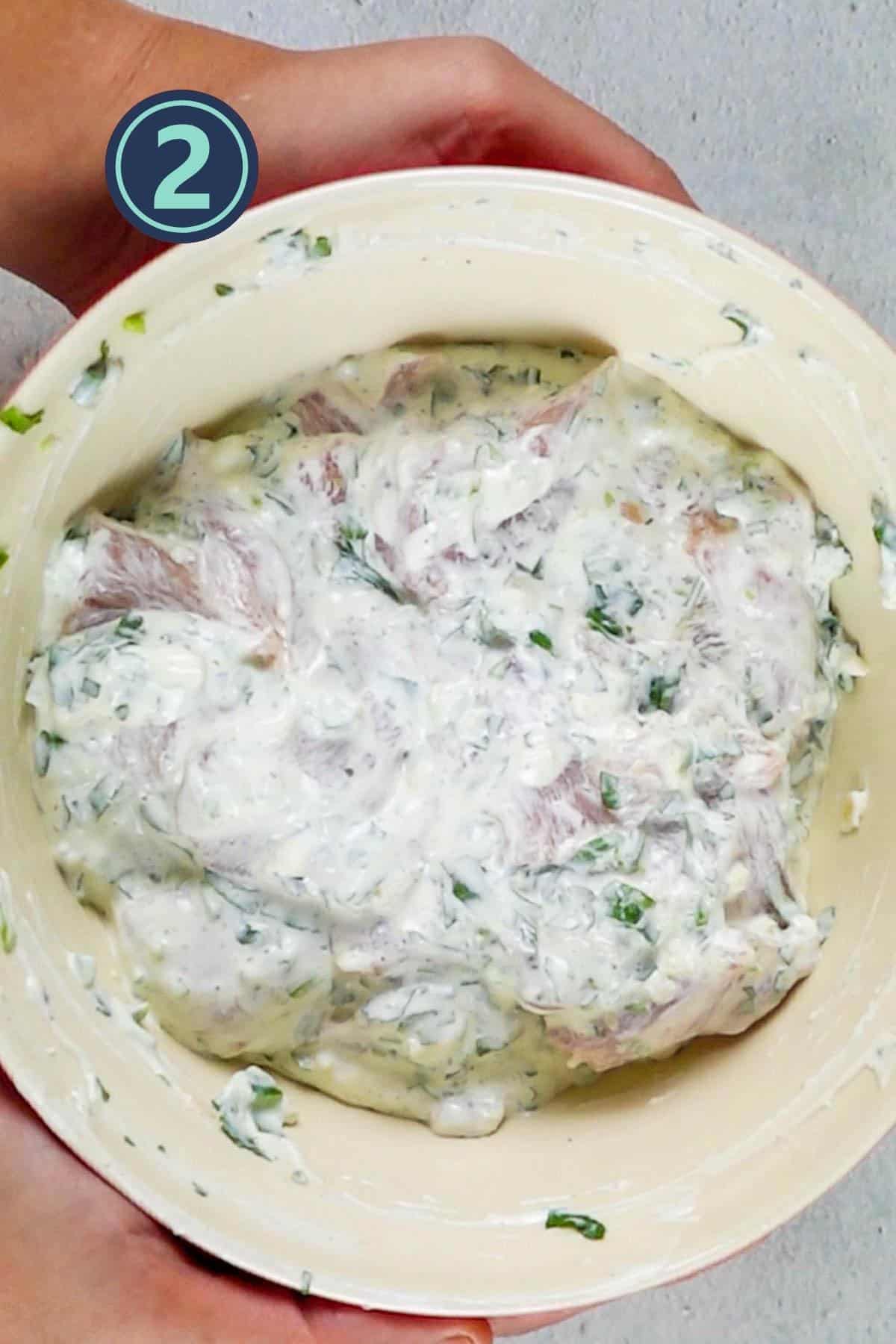 Chicken pieces for malai boti marinated in a large bowl.