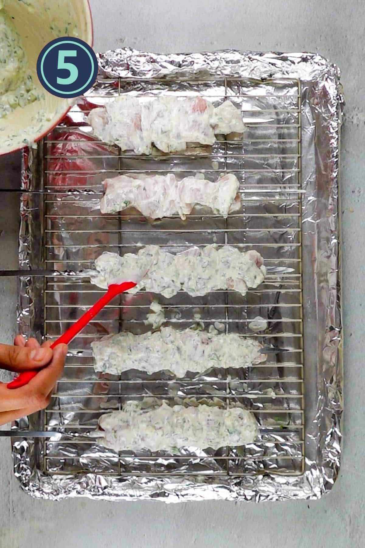 Applying malai boti marination on the chicken skewers.