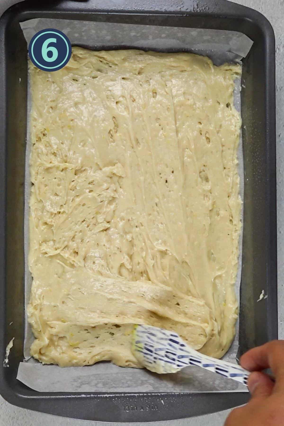 spreading a layer of blueberry cake batter into the cake pan.